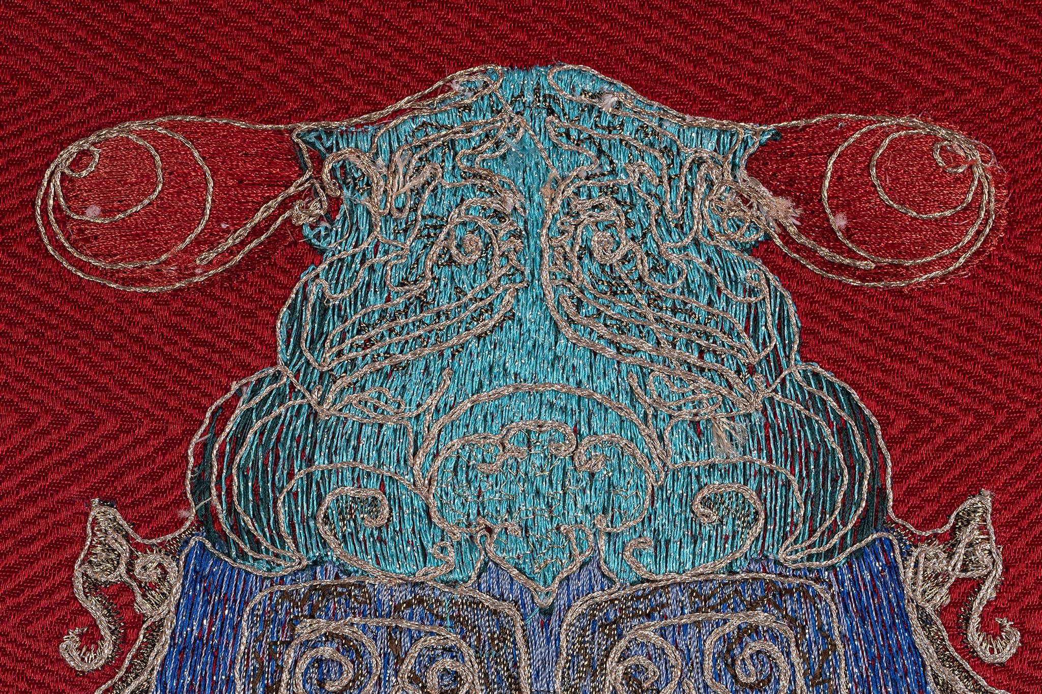 Close-up of the head details of a framed embroidery artwork featuring a cicada design.  The embroidery highlights detailed patterns in blue and white thread on a red background.