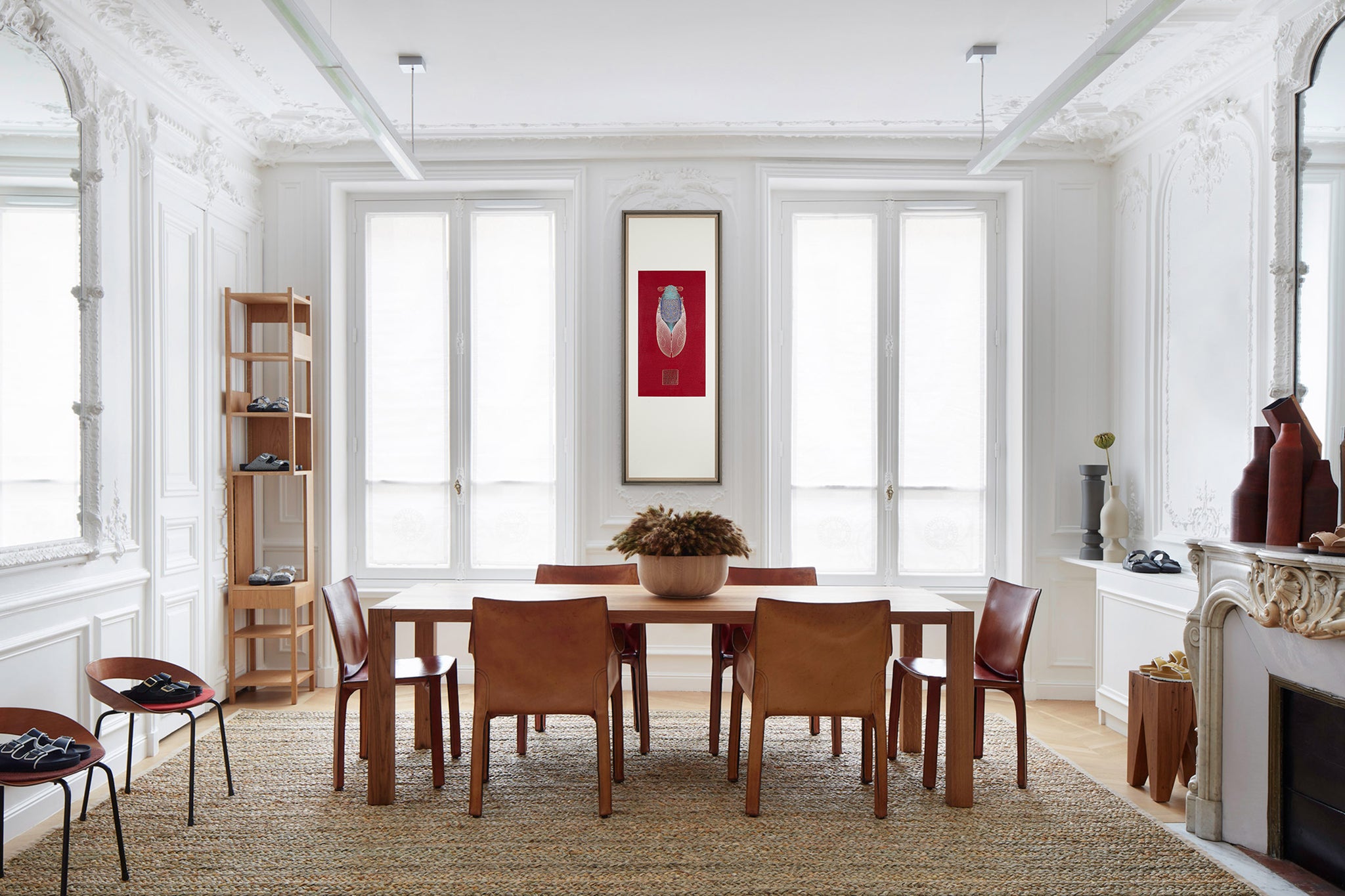 A modern dining room with a large table and chairs. A framed embroidery artwork featuring a cicada design hangs on the wall, adding a touch of elegance to the space.