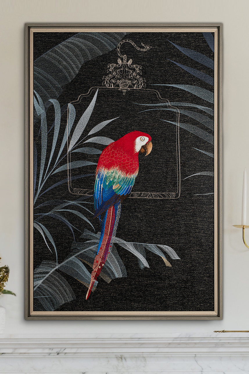 An embroidered macaw sits on a perch next to an embroidered artwork on a black background decorated with palm leaves.