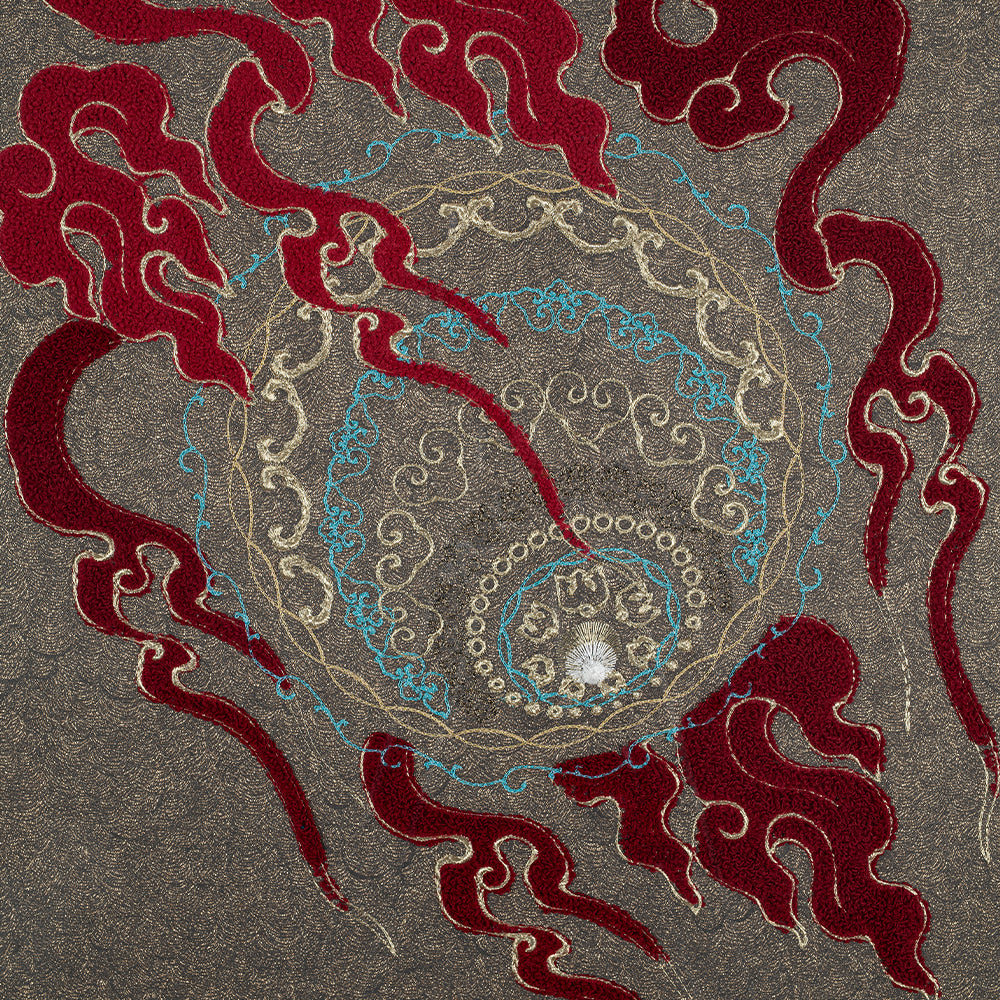 Intricate embroidery design featuring swirling patterns in red, blue, and gold threads on a grey background. The design includes abstract shapes and a central circular motif.