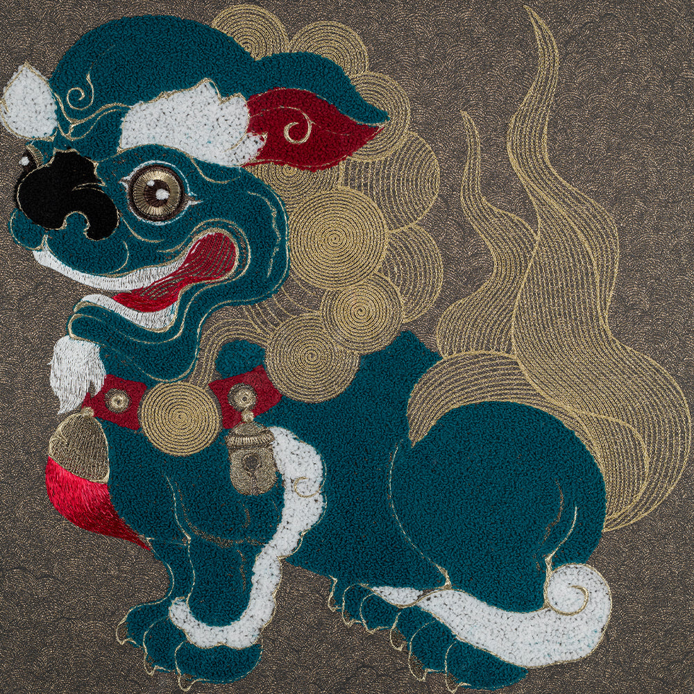 Embroidered artwork depicting a mythical creature resembling a lion with a curly mane. The creature is embroidered in teal, red, white, and gold threads on a dark grey background.