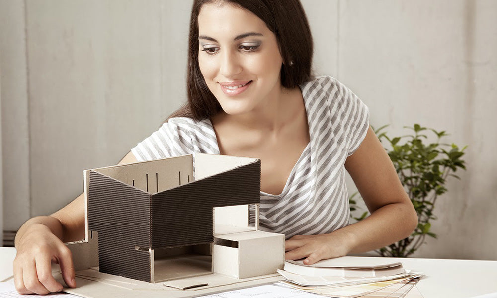 A female architect looking over a model house with blueprints and color swatches on the table.