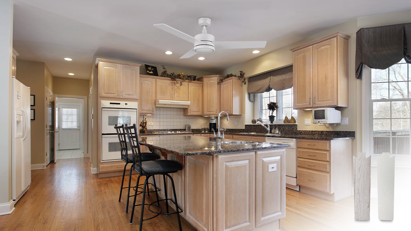 A spacious kitchen featuring a Louy 52-inch white ceiling fan with a light and wall switch. The kitchen has light wood cabinetry with a central island that includes a sink and seating with black bar stools. The countertops are dark granite, and there are stainless steel appliances including a double oven and a microwave mounted under a cabinet. The backsplash is white tile, and there are large windows with dark valances allowing natural light to enter.