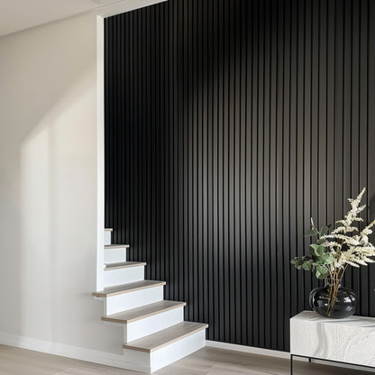 Black matte acoustic slat wall panels installed along a stairway, adding sleek, modern texture to the minimalist interior design.