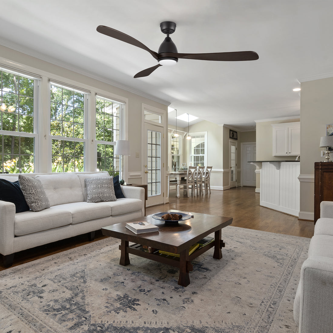 A Nephele ceiling fan with an integrated LED light, remote-controlled functionality, and a bold black finish, harmonizing perfectly with the cozy furnishings of a contemporary living room. 
