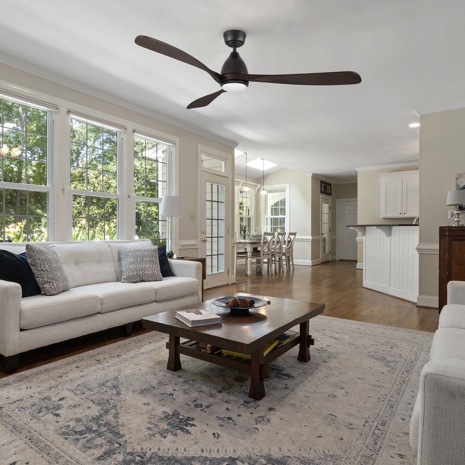 A Nephele ceiling fan with an integrated LED light, remote-controlled functionality, and a bold black finish, harmonizing perfectly with the cozy furnishings of a contemporary living room. 