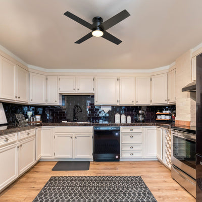A modern kitchen with white cabinets, dark tile backsplash, and 52 inch black flush-mount ceiling fan with an integrated LED light in the center of the ceiling. The kitchen features stainless steel appliances, dark countertops, and a patterned area rug on a wooden floor. #color_black
