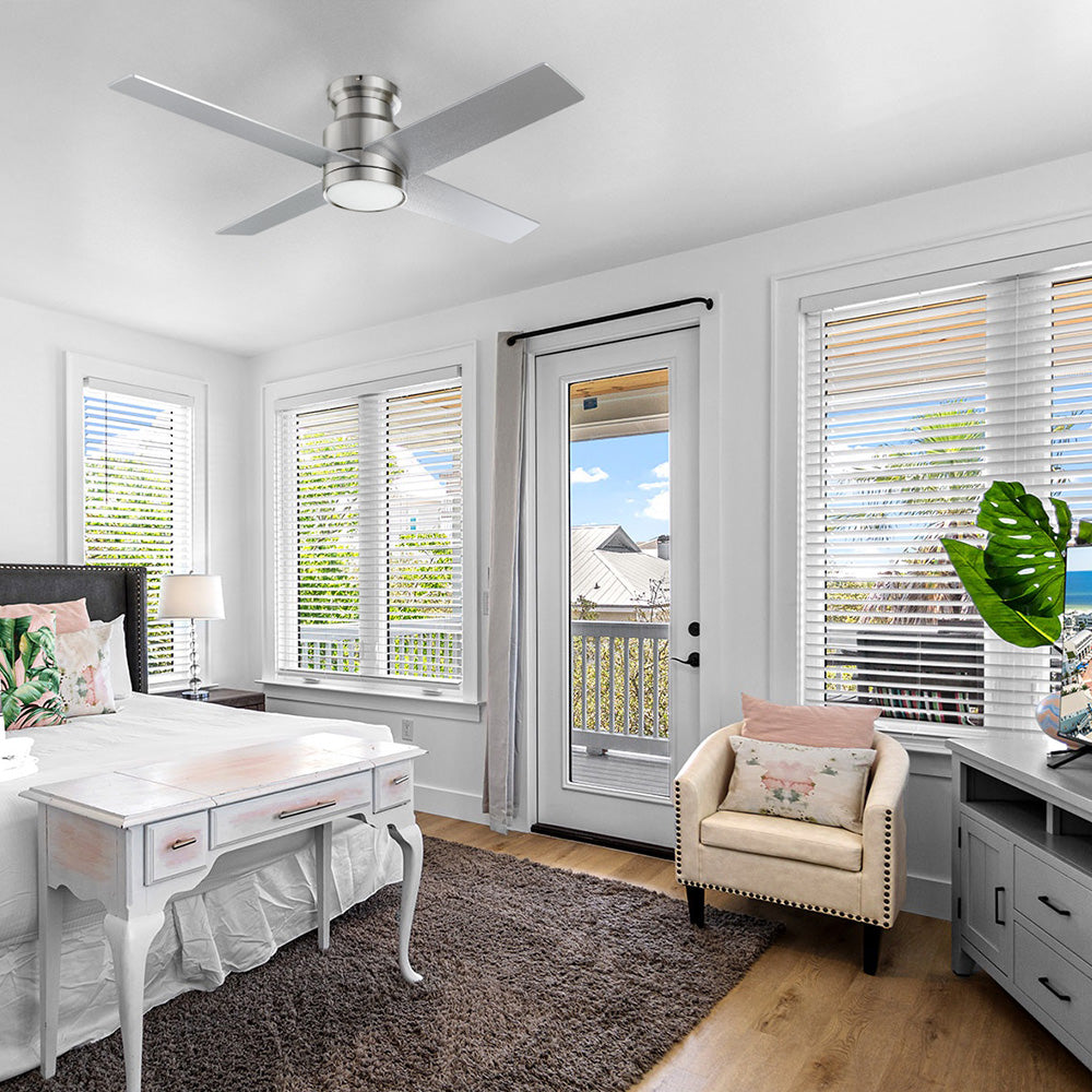 Traditional white-walled bedroom featuring a wooden desk, a plush armchair with a pink pillow, and a silver flush-mount ceiling fan in brushed nickel steel finish centered above a textured area rug. 