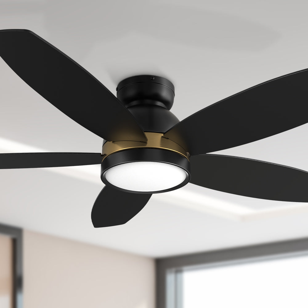 A black 48-inch Smafan Carro Povjeta outdoor smart flush mount ceiling fan with a light kit, featuring five black blades, a gold accent ring, and a round integrated light, installed on a white ceiling in a modern room with a window and beige walls. 