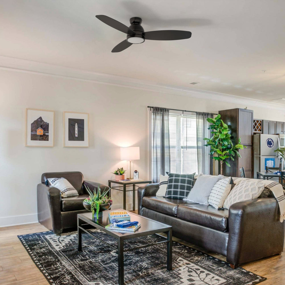 A modern living room featuring 52-inch black, flush mount ceiling fan with a light, showcasing its smart and modern design. The room also contains dark leather seating, a coffee table, and decorative elements. 