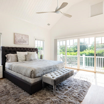 Nephele White wood ceiling fan with LED light installed on a vaulted ceiling in a modern master bedroom with a large sliding glass door. 
