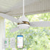 A Smafan Biscay2 outdoor smart white ceiling fan with light, featuring five white blades, installed in a covered outdoor space with large windows and white curtains.  The fan has a gold accent ring.  Below, three control methods are shown: a wall-mounted control labeled "CARRO" with multiple buttons, a handheld remote with similar functionality, and a smartphone displaying a smart fan control app interface.  The background shows a lush green outdoor view. 