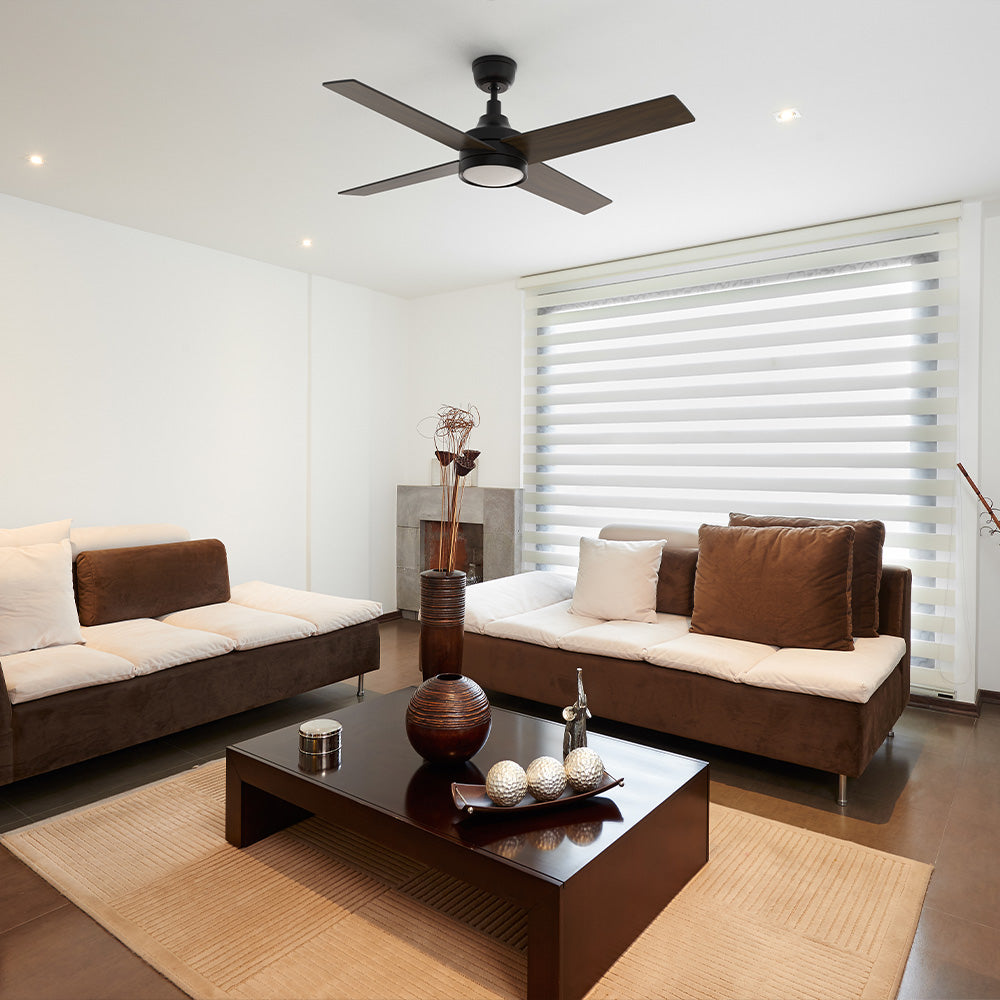 Smafan Bryant black ceiling fan with light installed in a contemporary minimalist living room with brown and white sofas, a dark wood coffee table, and large window blinds. 