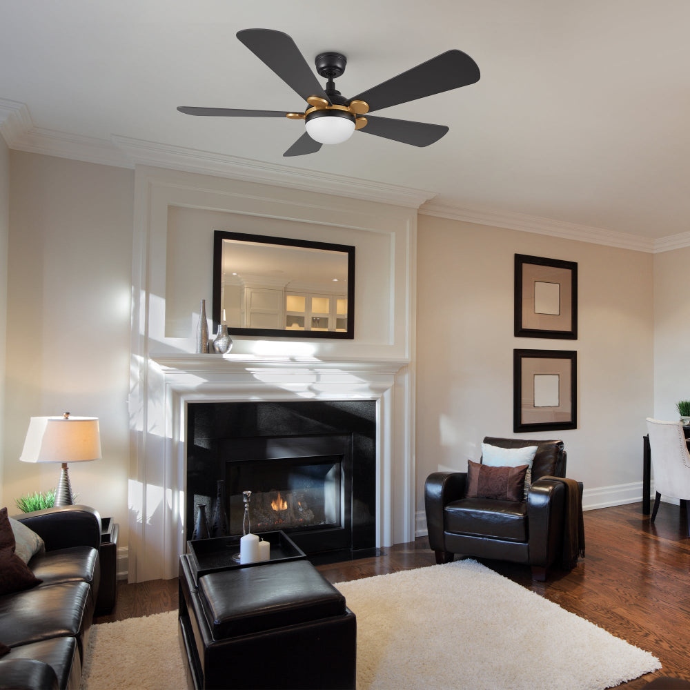 Lille 52 inch black and gold five-blade ceiling fan with an integrated LED light hangs from the ceiling in a living room with a fireplace and dark leather furniture. 