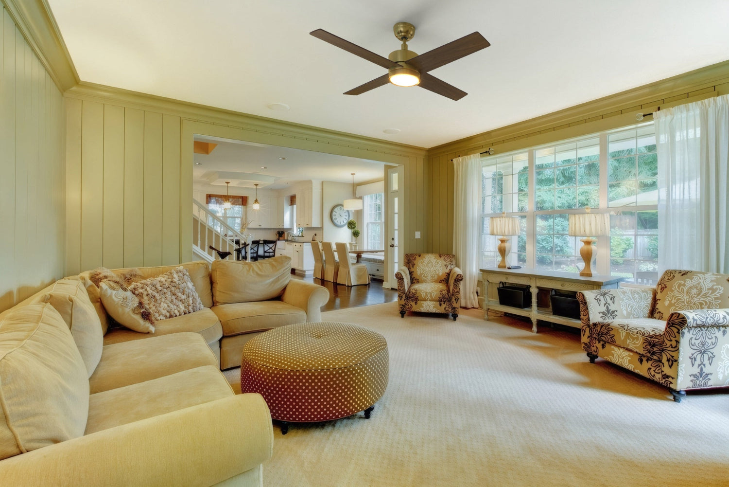 Modern living room featuring a Smafan Rossendale 52-inch gold ceiling fan with integrated bright LED light, beige sectional sofa, patterned armchairs, round ottoman, and large windows with sheer curtains allowing natural light.