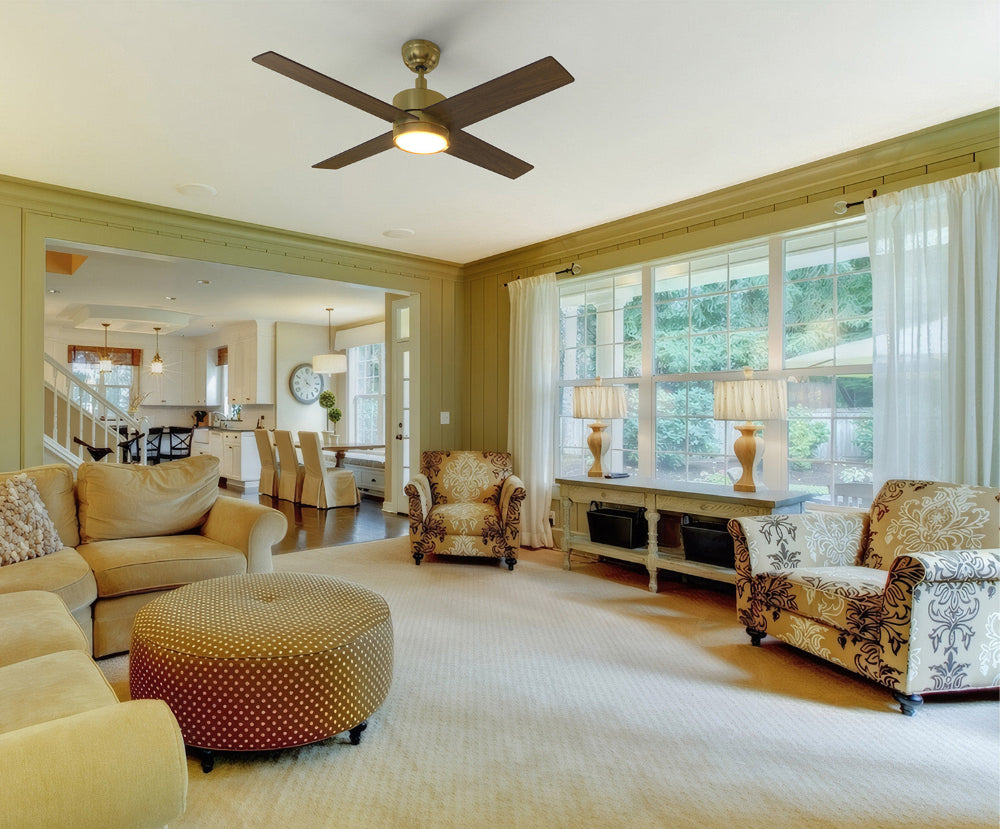 Modern living room featuring a Smafan Rossendale 52-inch gold ceiling fan with integrated bright LED light, beige sectional sofa, patterned armchairs, round ottoman, and large windows with sheer curtains allowing natural light. 