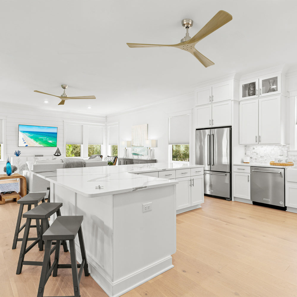 Smafan Thora 60 inch ceiling fan with remote, modern open-concept kitchen and living room featuring white cabinetry, large island with dark stools, stainless steel appliances, light wood flooring, shiplap accent wall with blue and white artwork, and two gold ceiling fans overhead. 