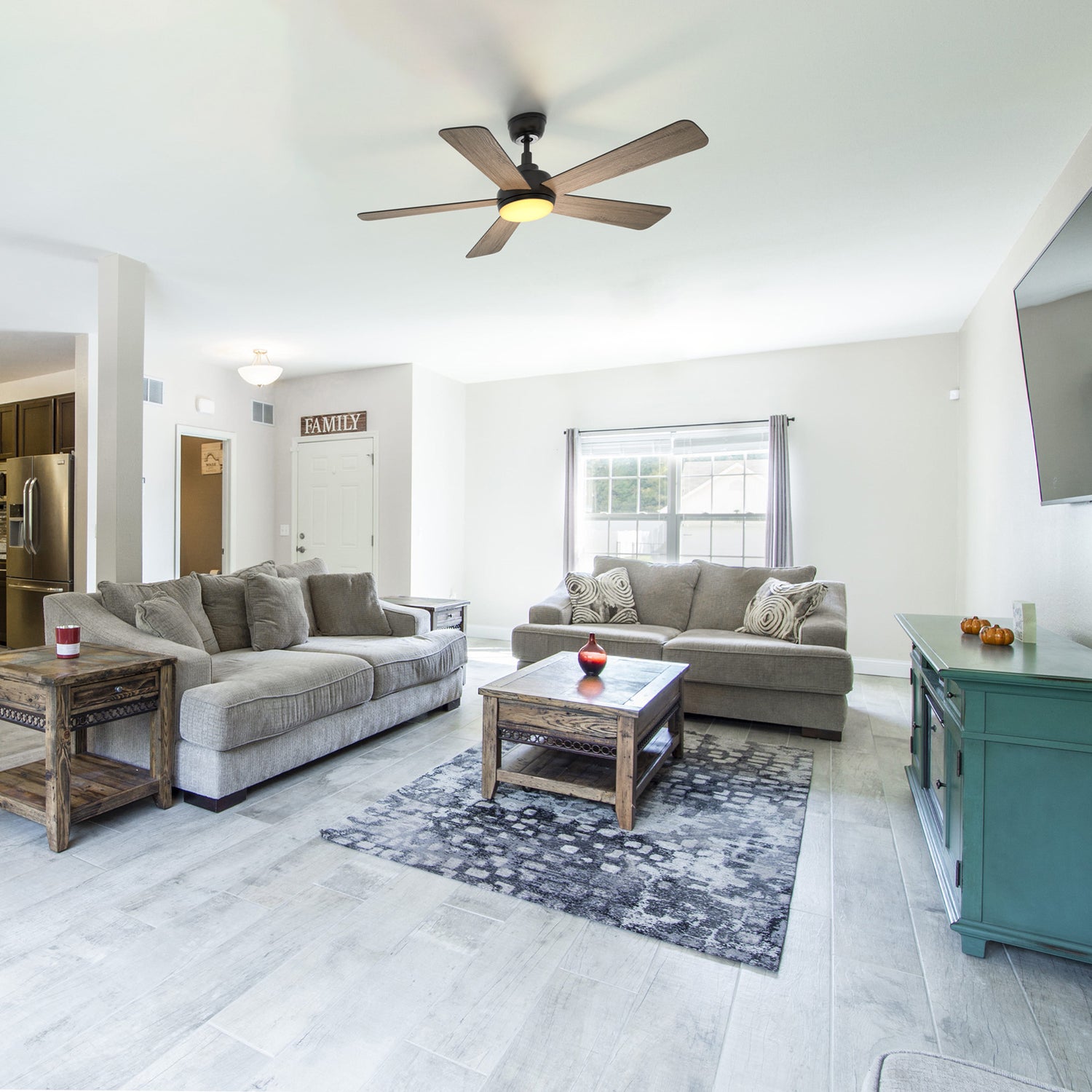 Smafan Toplam 52 inch wood ceiling fan with light is installed in a traditional living room featuring gray sofas, a rustic wood coffee table, and a dark patterned rug on tiled flooring. Large windows with drapes bring in natural light, complemented by a turquoise media console and warm decorative accents. 