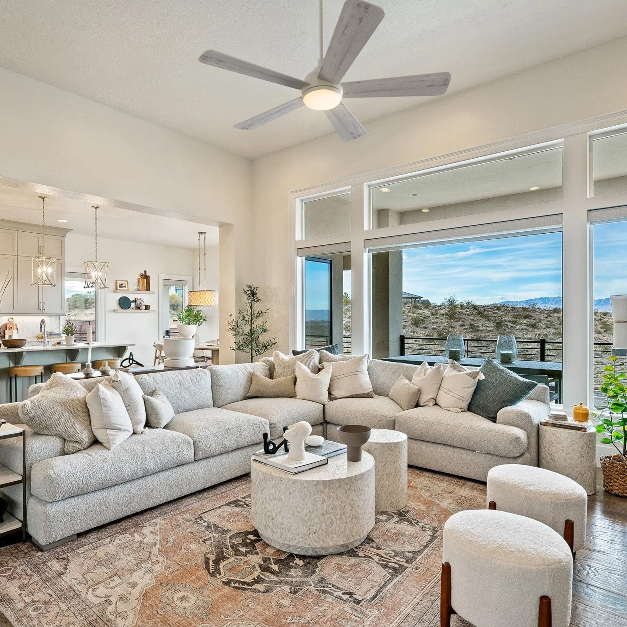 Smafan Toplam 52 inch white ceiling fan with light in a modern farmhouse living room featuring a large sectional sofa, round coffee tables, expansive windows with desert views, and an open entryway to the kitchen. 