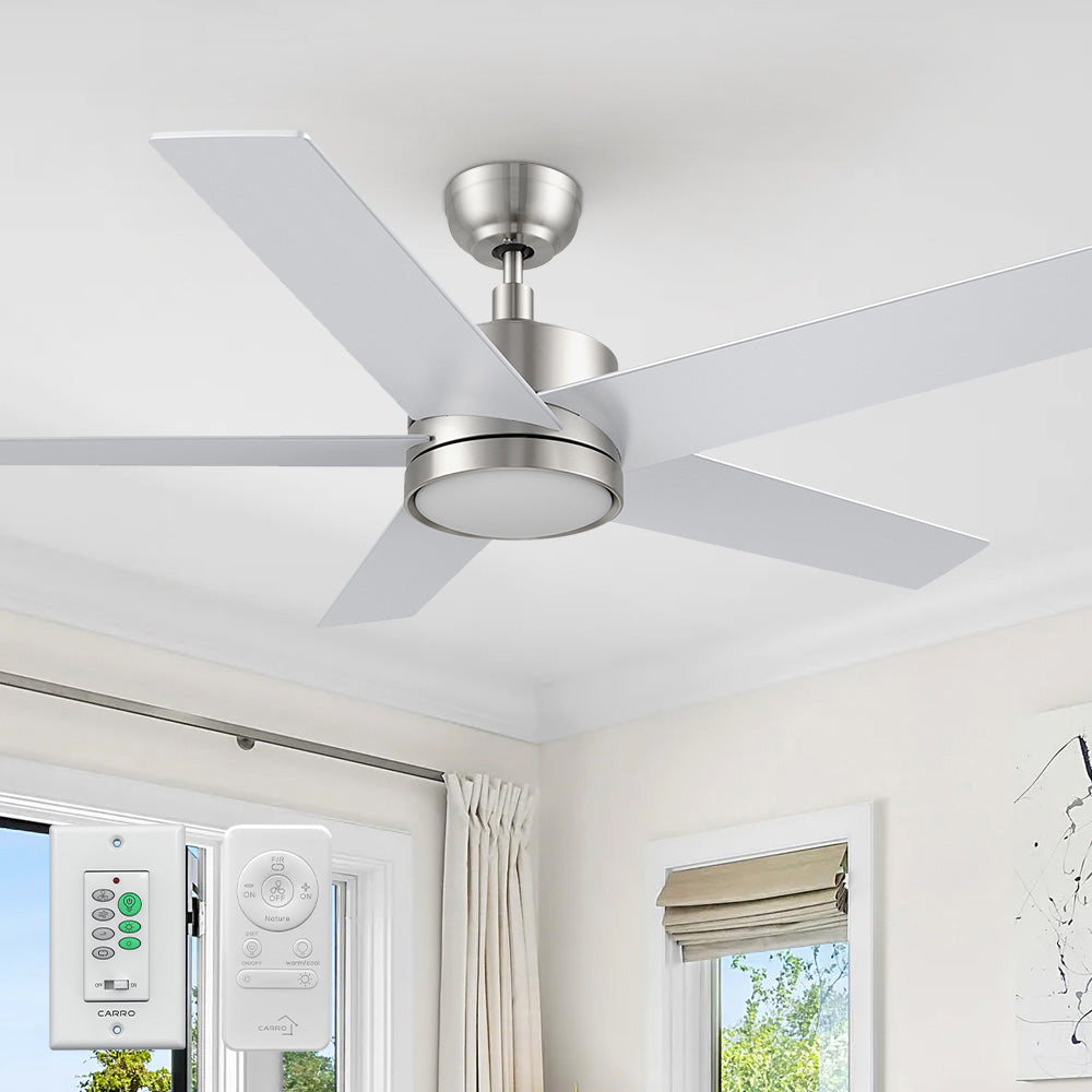 A modern 52-inch Smafan Trafford2 brushed nickel ceiling fan with light, featuring five white blades, installed in a bright room with beige curtains and a roman shade. Two control ways are shown below: a wall control labeled &quot;CARRO&quot; with multiple buttons for fan and light settings, and a handheld remote with similar functionality. 