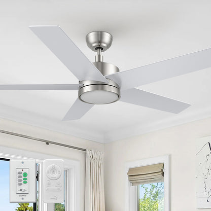 A modern 52-inch Smafan Trafford2 brushed nickel ceiling fan with light, featuring five white blades, installed in a bright room with beige curtains and a roman shade. Two control ways are shown below: a wall control labeled &quot;CARRO&quot; with multiple buttons for fan and light settings, and a handheld remote with similar functionality. 