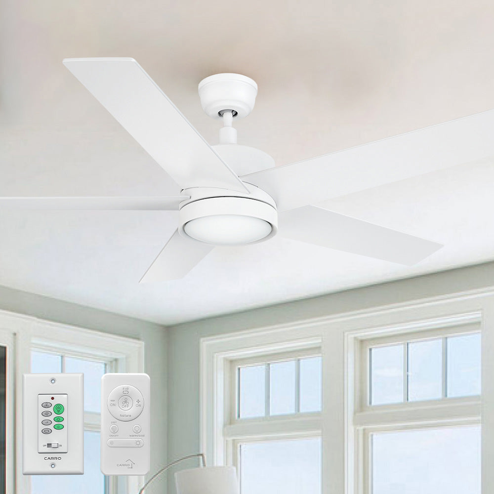 A modern 52-inch Smafan Trafford2 white ceiling fan with a 
 light, featuring five white blades, installed in a bright room with large windows and white trim. Two control methods are shown below: a wall control labeled "CARRO" with multiple buttons for fan and light settings, and a handheld remote with similar functionality. 