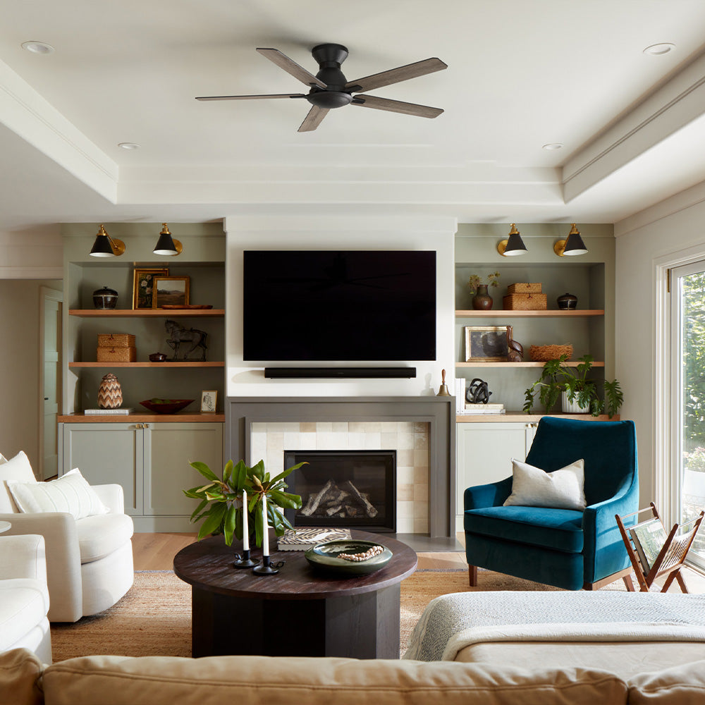 A modern living room with a built-in fireplace and wall-mounted TV, styled with neutral seating and a teal accent chair. Flush mount ceiling fan with wood-tone blades hangs overhead, providing quiet airflow and balanced comfort for a spacious indoor living area. 