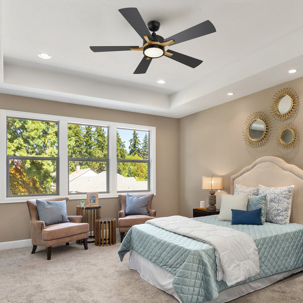 A bright and cozy bedroom featuring neutral-toned walls, a tufted beige headboard, and coordinated bedding in soft blue and white. The room includes accent chairs by the window, nightstands with lamps, and decorative wall mirrors. A Smafan Apex 52-inch smart ceiling fan with LED light is mounted on the tray ceiling, adding comfort and a modern touch. 