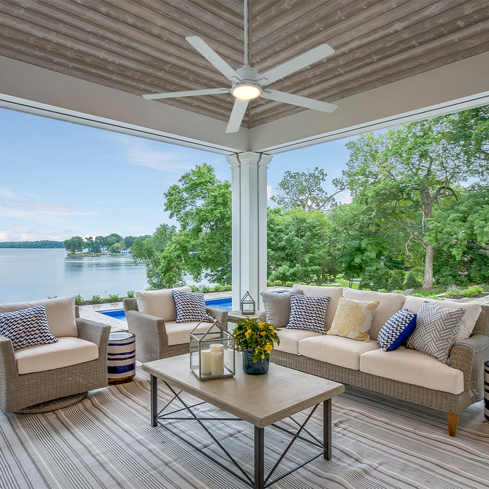 Smafan Essex 56 inch white outdoor ceiling fan with LED light installed on a covered lakeside patio. The modern fan complements the open-air living space with wicker seating, a pool view, and scenic waterfront surroundings, delivering comfortable airflow for outdoor relaxation and entertaining. 