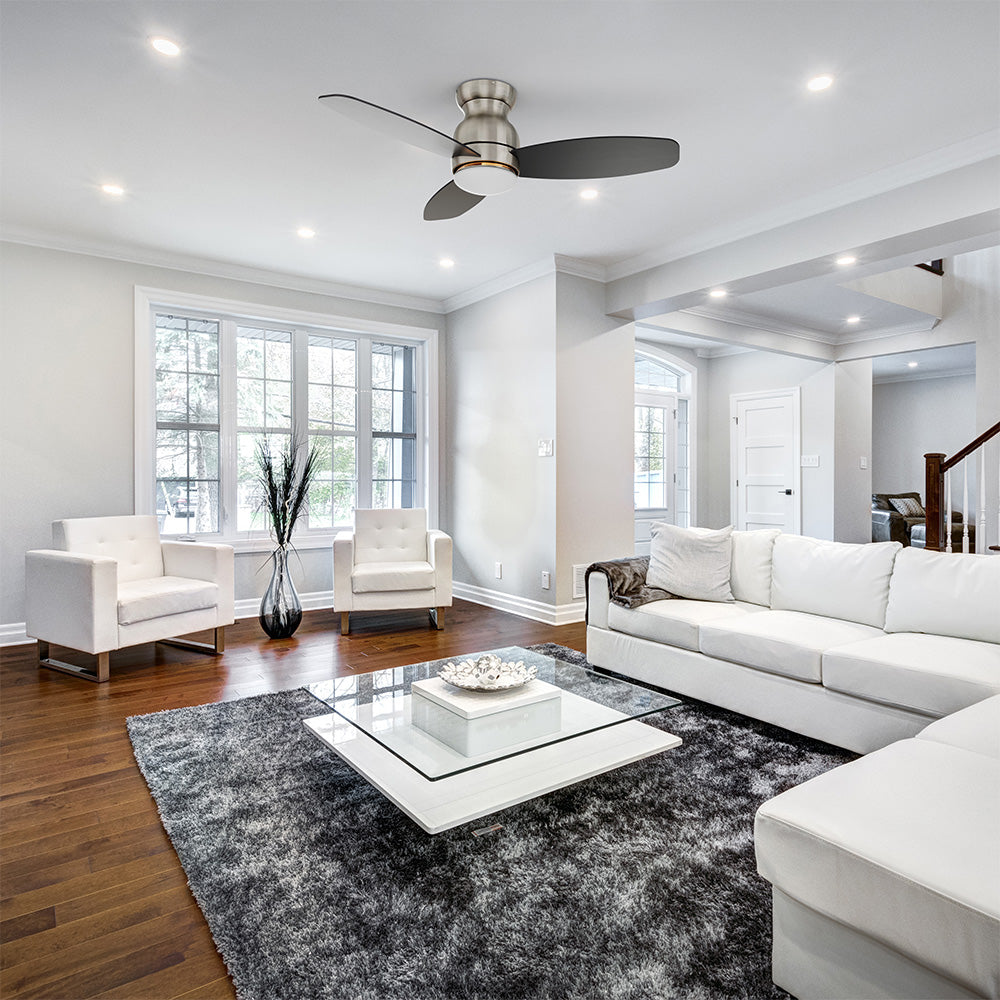 The sleek living room features a modern interior design with key furniture pieces including a glass-top coffee table with a white base, a white sectional sofa with a chaise, and 3-blade Brushed Nicke flush mount ceiling fan with LED light. 