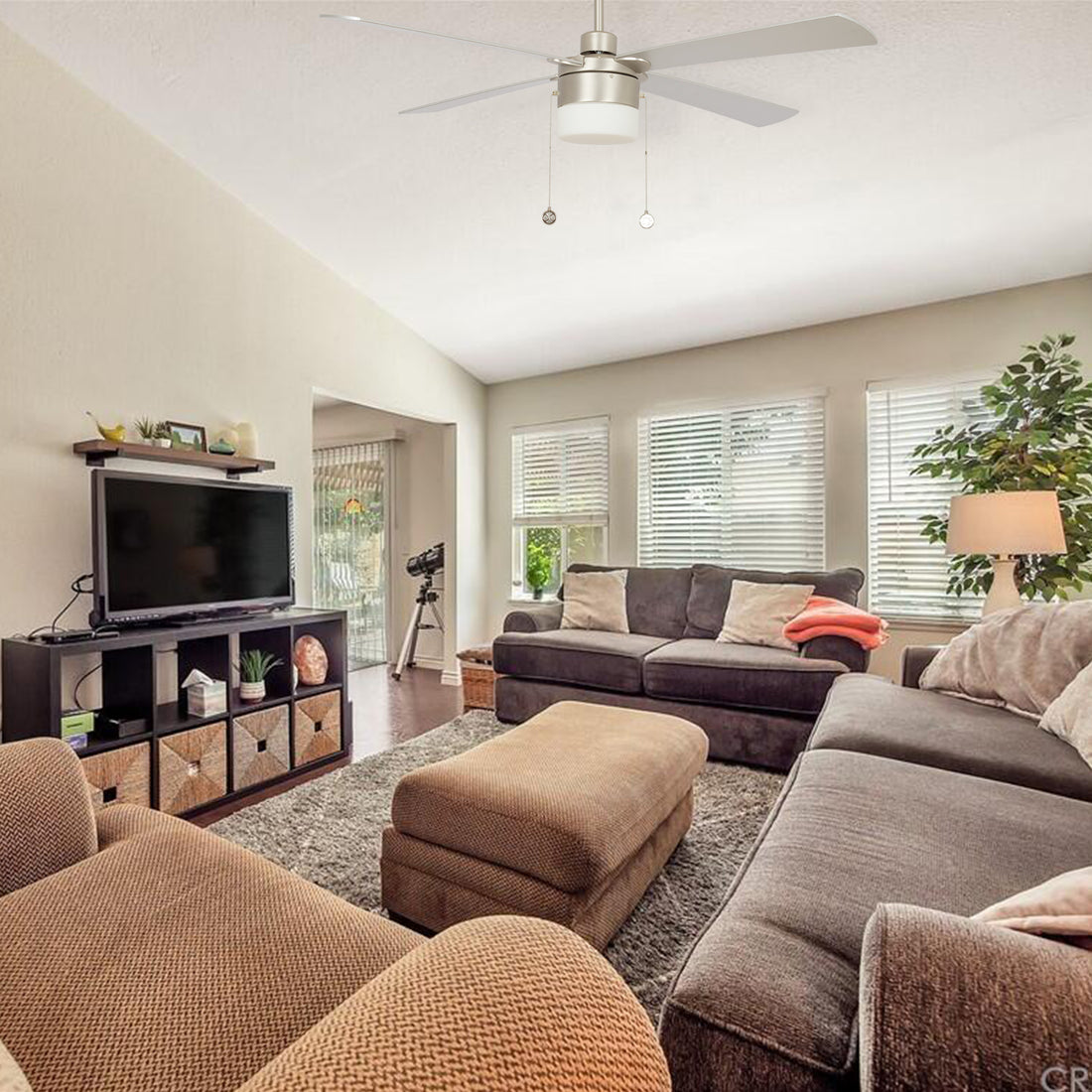 Brushed nickel ceiling fan with drum light and pull chains in a living room with vaulted ceiling and gray sofas. 