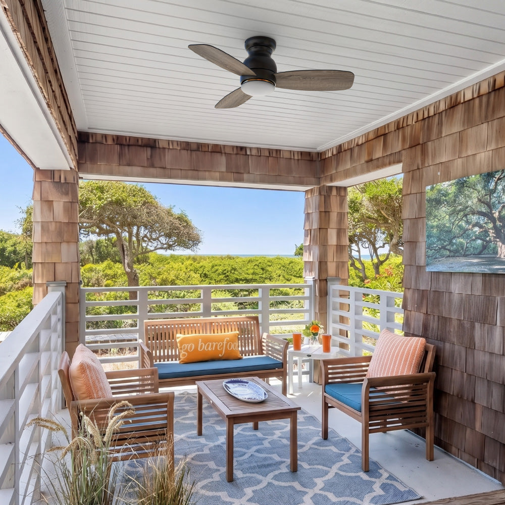 Flush mount ceiling fan with light and dark wood grain blades, mounted in a coastal style outdoor porch seating area. 